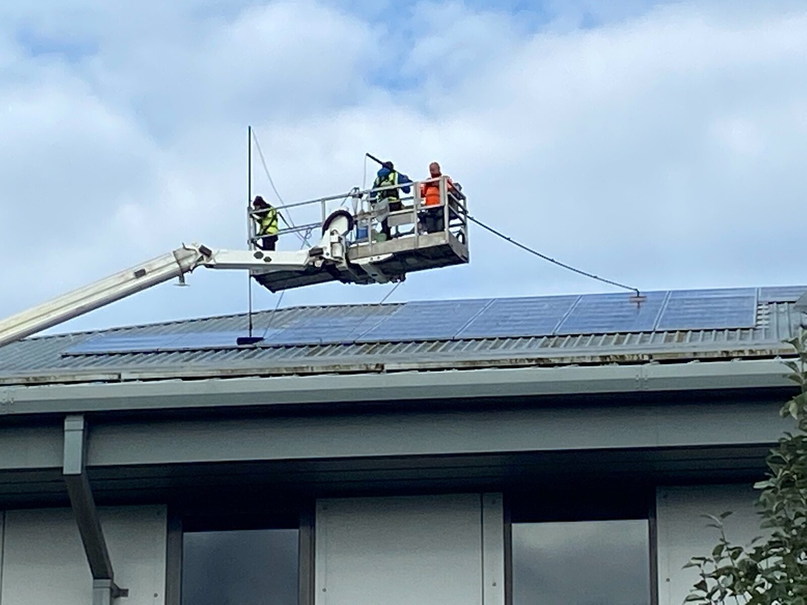 Commercial rooftop solar panel cleaning team using a boom lift