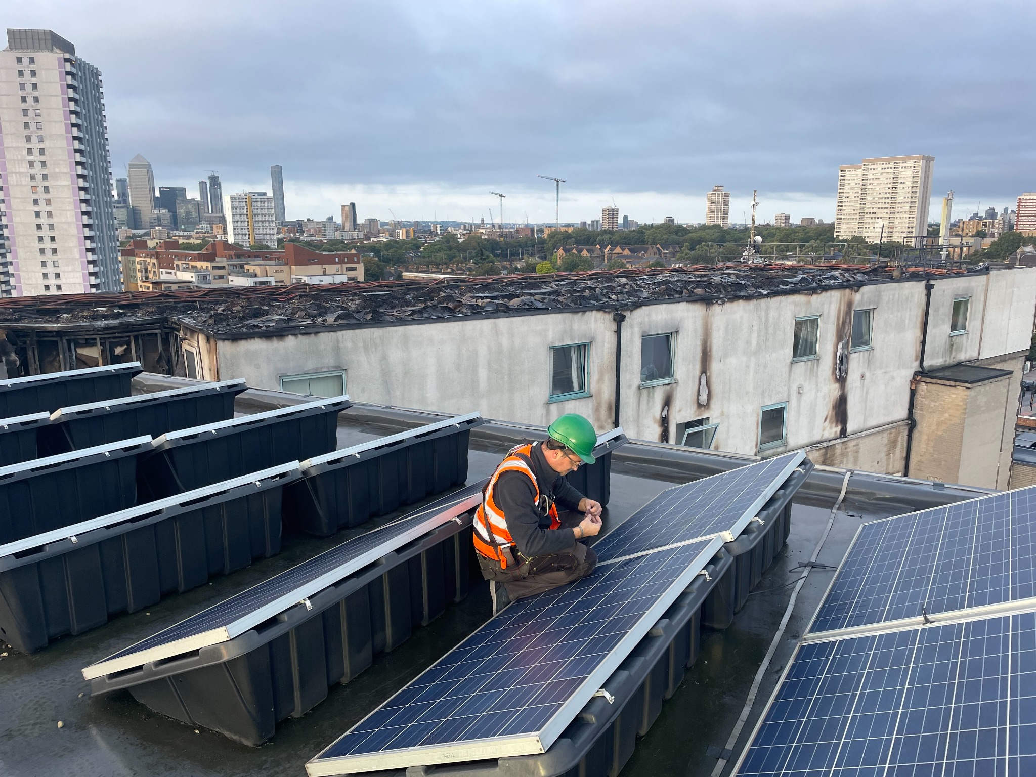 Solar specialist assessing photovoltaic modules beside a fire-damaged rooftop